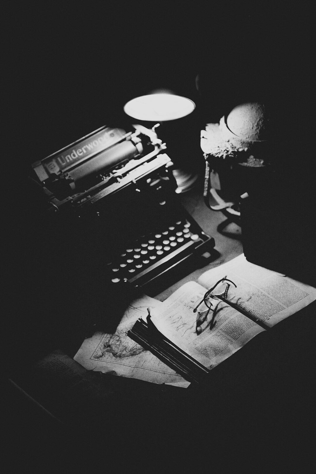 Vintage typewriter with magnifying glass and old notebook on a wooden desk under warm lamp light